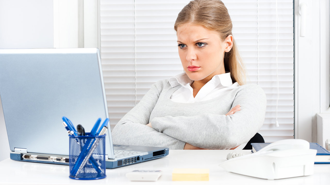 Eine junge Frau schaut in den Laptop und ärgert sich, weil sie in einer Behörde arbeitet und gendern soll. Gender-Verweigerung