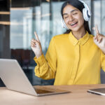 Ein junge Frau mit Kopfhörern und Laptop hört während der Arbeit Musik.