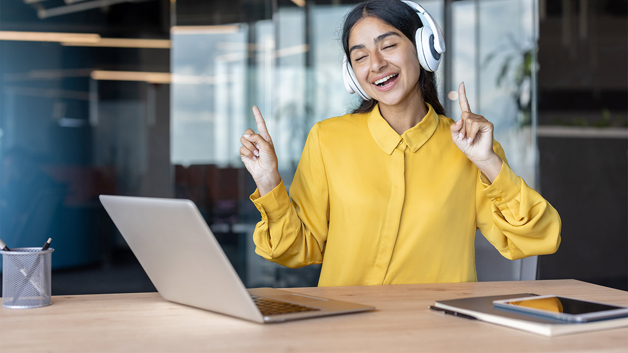 Ein junge Frau mit Kopfhörern und Laptop hört während der Arbeit Musik.