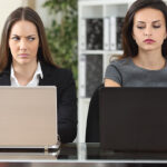 Zwei Frauen mit Laptop vertrauen sich nicht. Verbale No-Gos am Arbeitsplatz