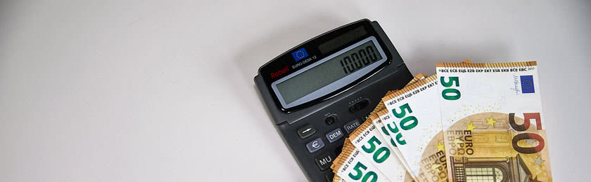Ein Taschenrechner mit mehreren 50€ Scheinen. Auf dem Display erscheint eine berechnete Abfindung von 10.000 Euro.