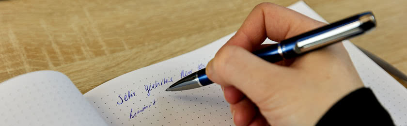Mit der rechten Hand wird eine schriftliche Kündigung auf Papier niedergeschrieben.
